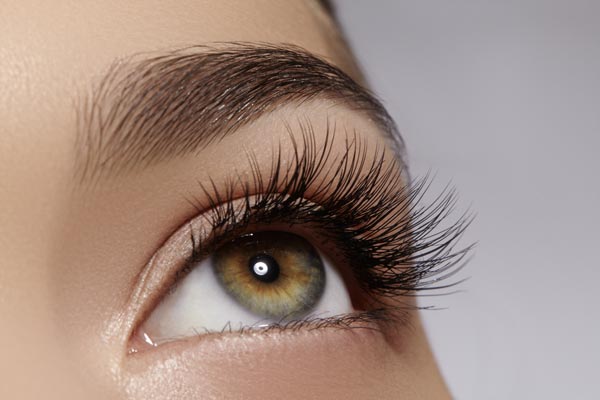 close up image of a beautiful blue and green iris with long eyelashes and manicured eyebrows