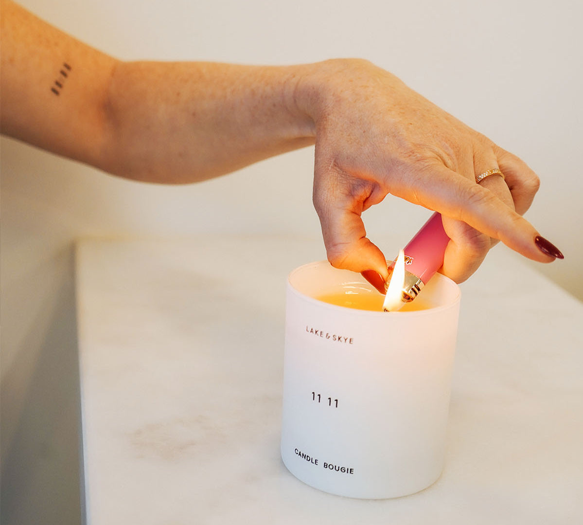 a hand lighting a 11:11 lake and skye candle on a marble surface