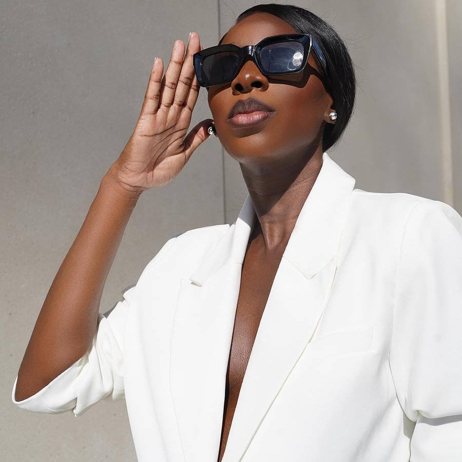 woman wearing white suit and large black sunglasses looking into the sun