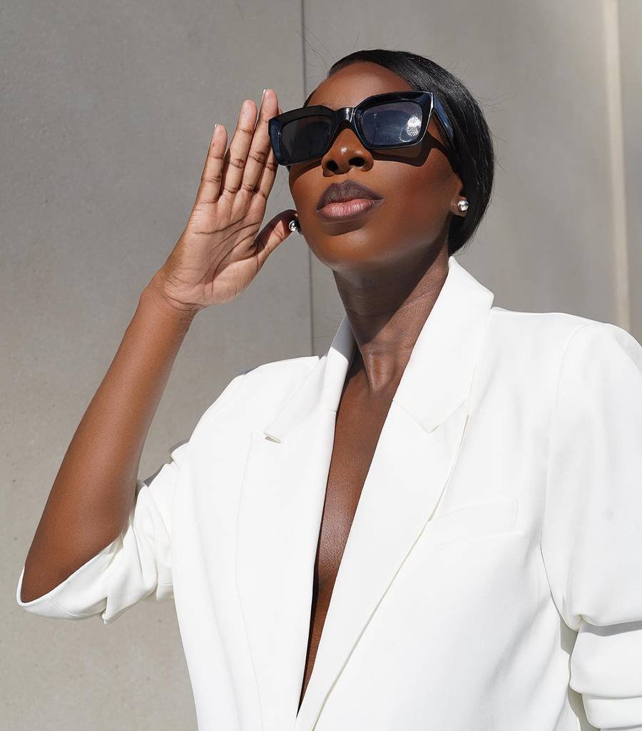 woman wearing white suit and large black sunglasses looking into the sun