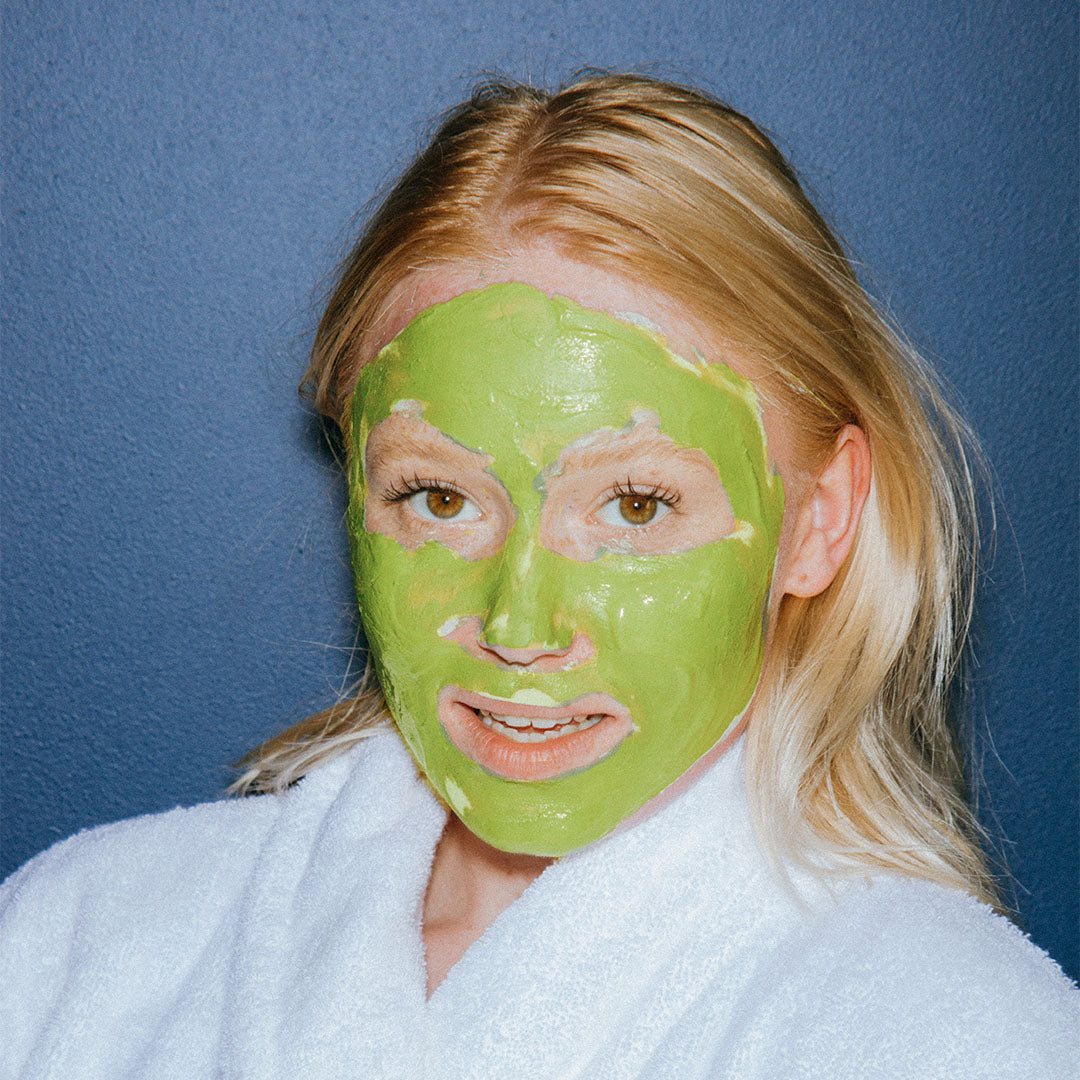 a blonde woman wearing a green skin care face mask treatment