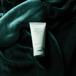 Tube of Night Zyme skincare product on a dark green fabric background